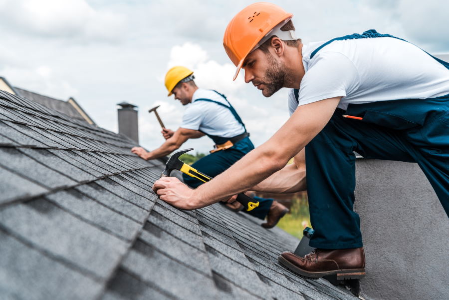 Roofing contractors repairing shingles on a rooftop with hammers and hard hats